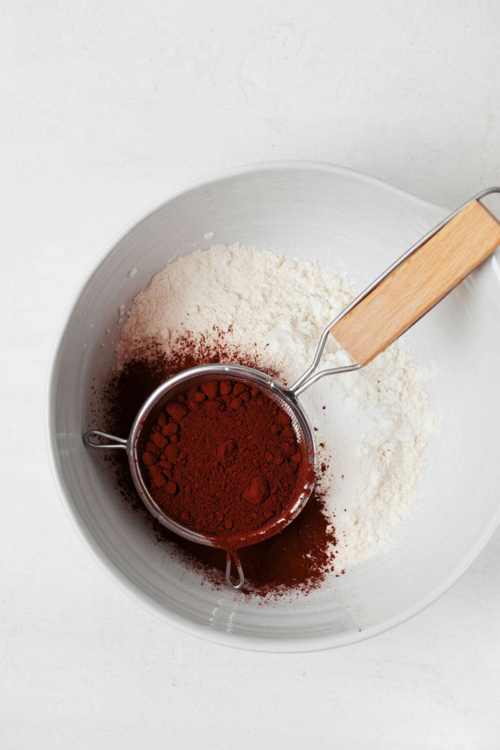 A white mixing bowl has been filled with flour and sifted cocoa powder.