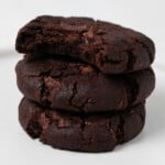 A stack of thick, chewy vegan double chocolate chip cookies is resting on a white plate.