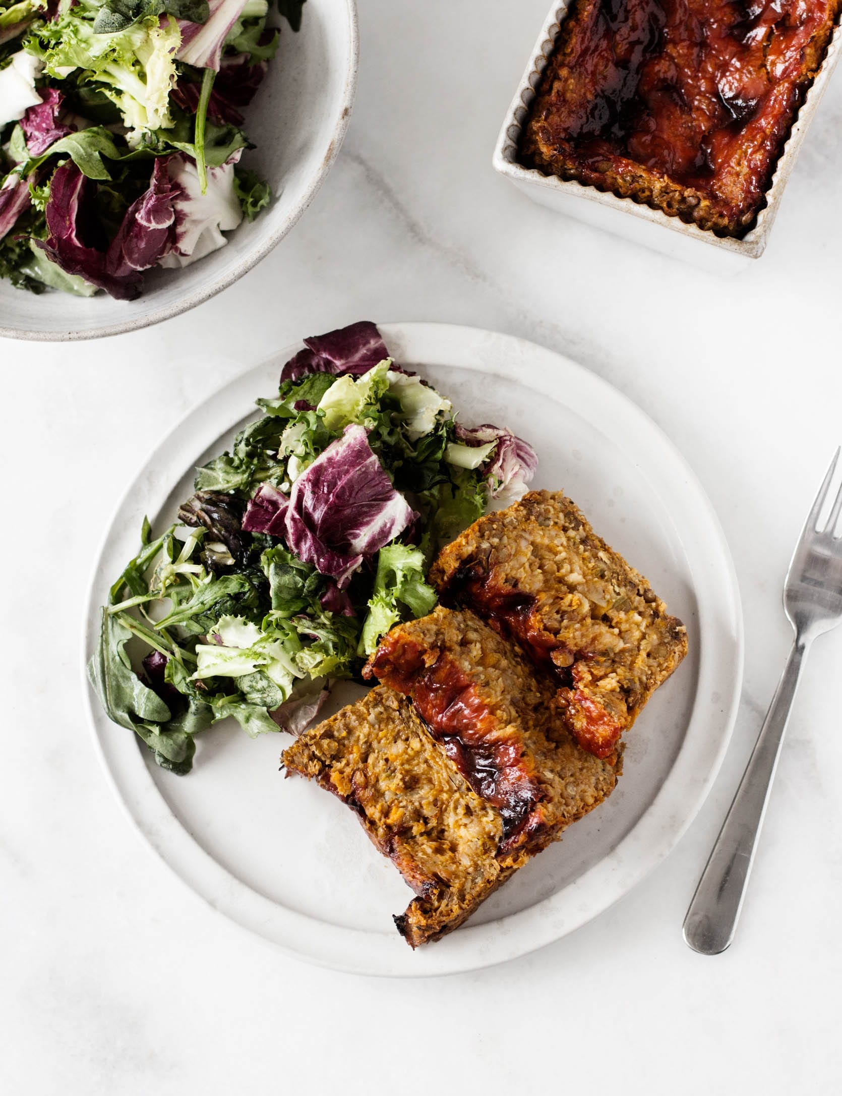 Freshly cut slices of vegan lentil sweet potato loaf, served with a side salad for a meal.