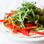 An angled photo of a tortilla pizza, which is covered in arugula and peppers.