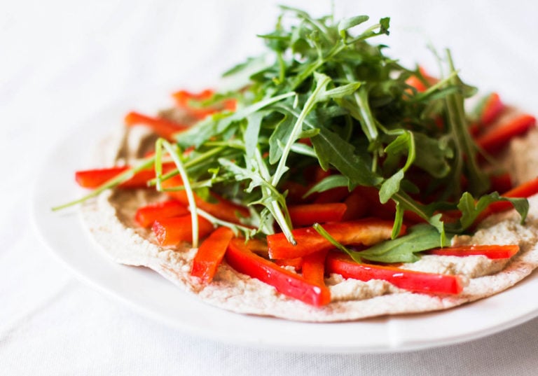 An angled photo of a tortilla pizza, which is covered in arugula and peppers.