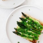 Two small, white appetizer plates carry a vegan green pea hummus tartine, topped with lemon zest and fleur de sel.