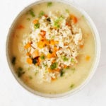 An overhead image of a white bowl, containing vegan avgolemono soup and flecked with green dill.