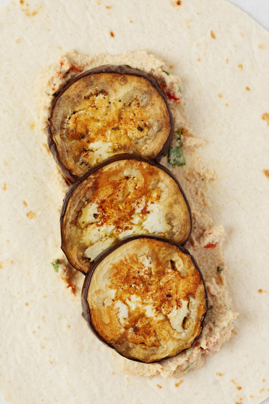 Round, roasted pieces of eggplant have been piled into a wheat wrap.