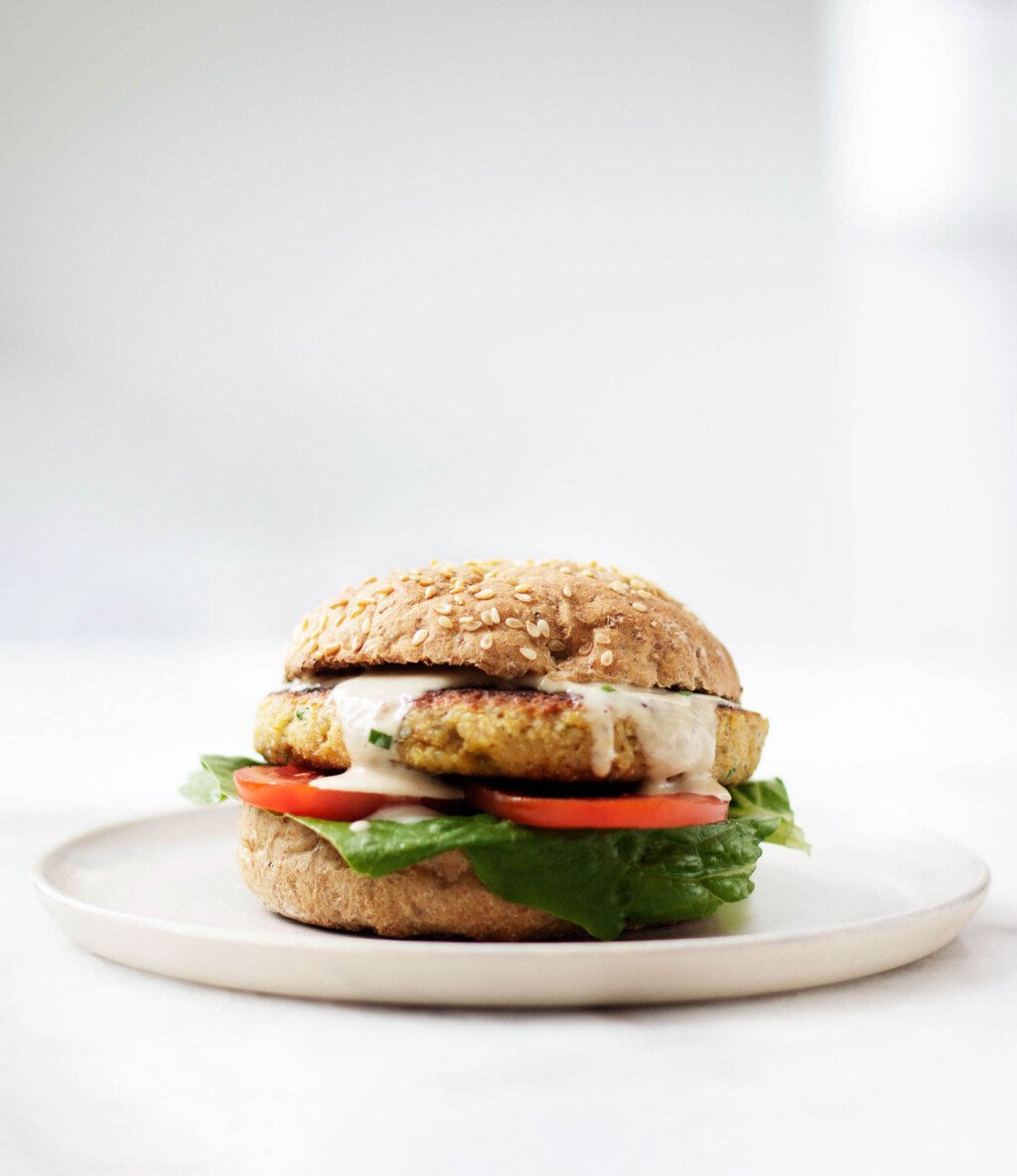 An image of a plump, crispy chickpea quinoa burger, which is piled onto a toasted bun with lettuce, tomato, and a creamy dressing.