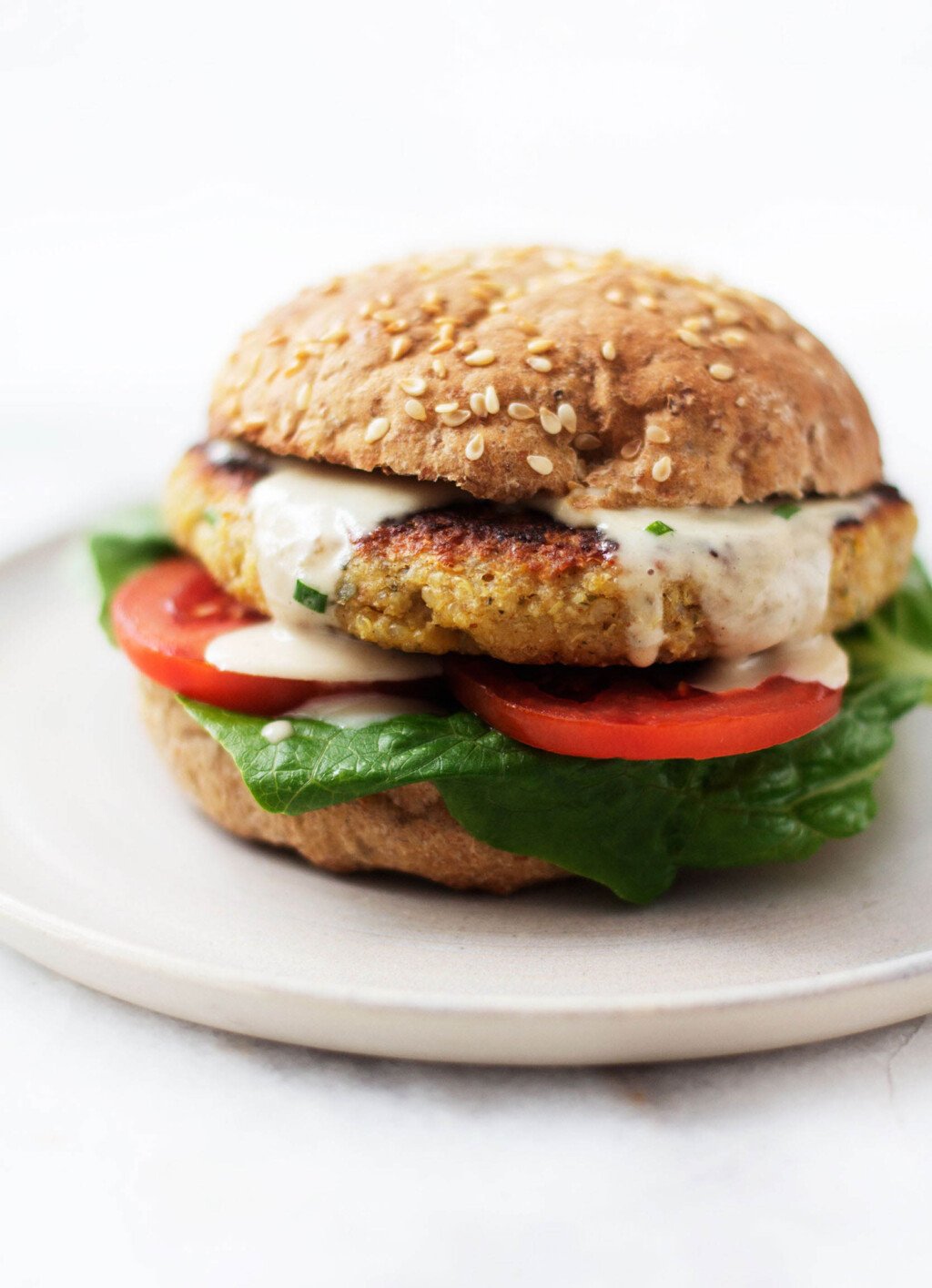 An image of a plump, crispy chickpea quinoa burger, which is piled onto a toasted bun with lettuce, tomato, and a creamy dressing.