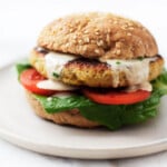 An image of a plump, crispy chickpea quinoa burger, which is piled onto a toasted bun with lettuce, tomato, and a creamy dressing.