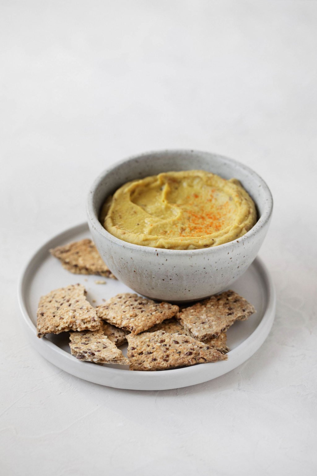 An angled image of a small appetizer plate with crackers and a dip. It rests on a white surface.