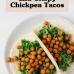 Two creamy kale and crispy chickpea tacos have been arranged on a round, white rimmed plate.