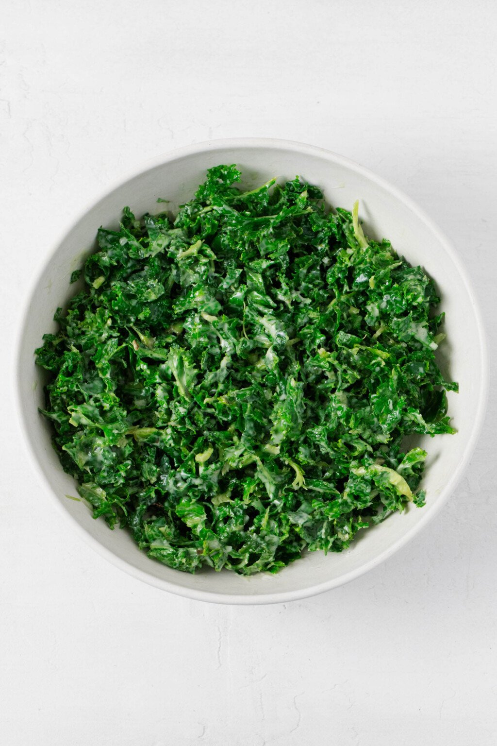 Raw, "massaged" kale with a creamy dressing is pictured in a white bowl. 