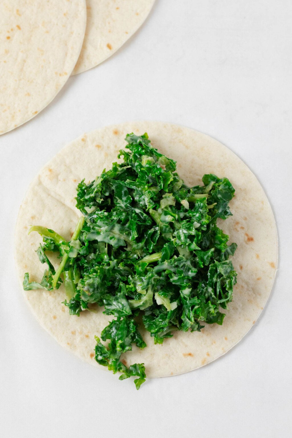 Green kale with a creamy dressing has been stuffed into a soft taco.