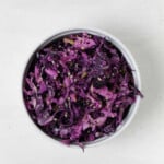 An overhead image of a crunchy slaw of apple and red cabbage, which is held in a small white bowl.