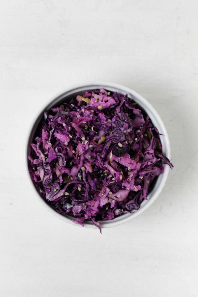 An overhead image of a crunchy slaw of apple and red cabbage, which is held in a small white bowl.