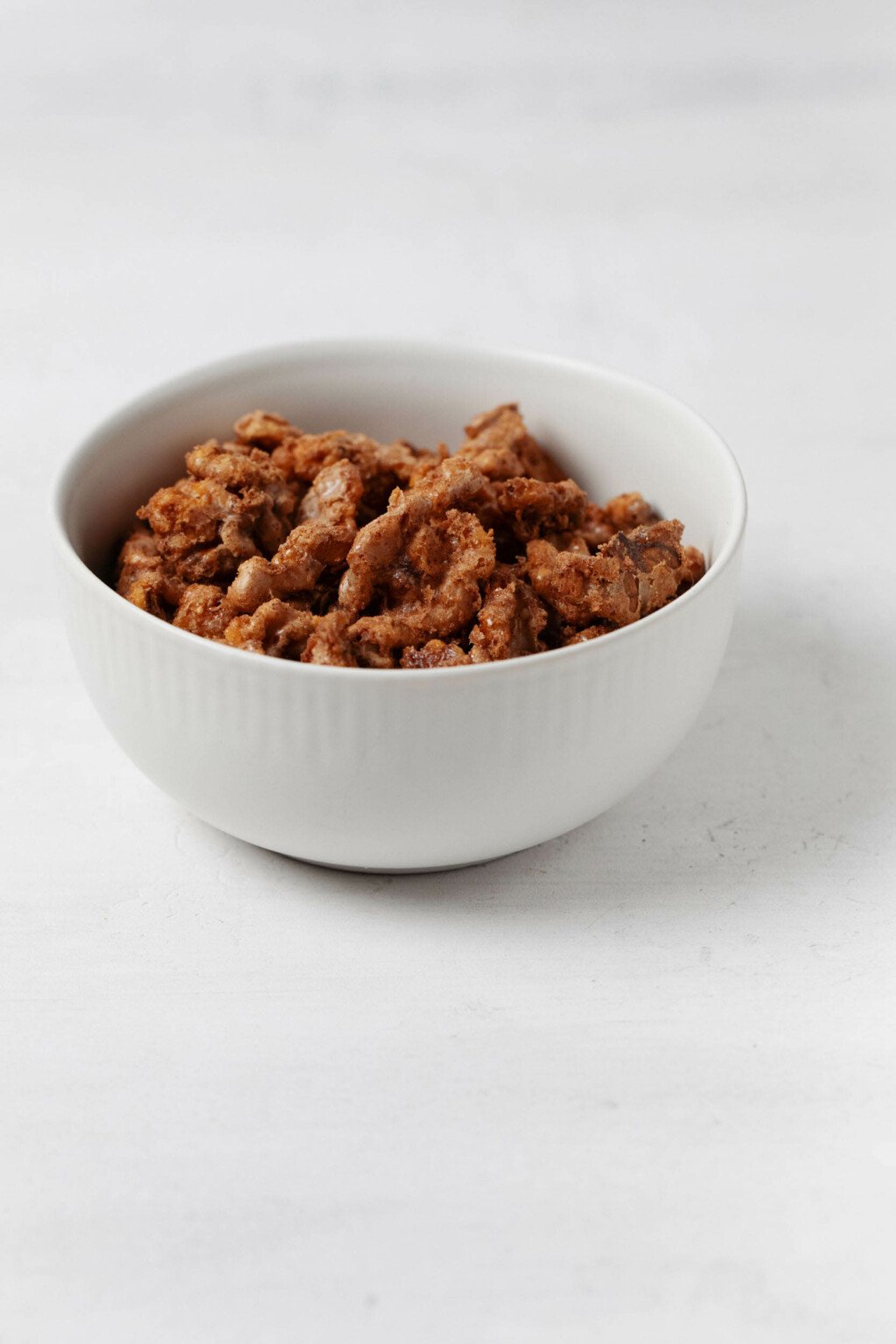A small, round white bowl holds crispy, baked vegan candied walnuts.