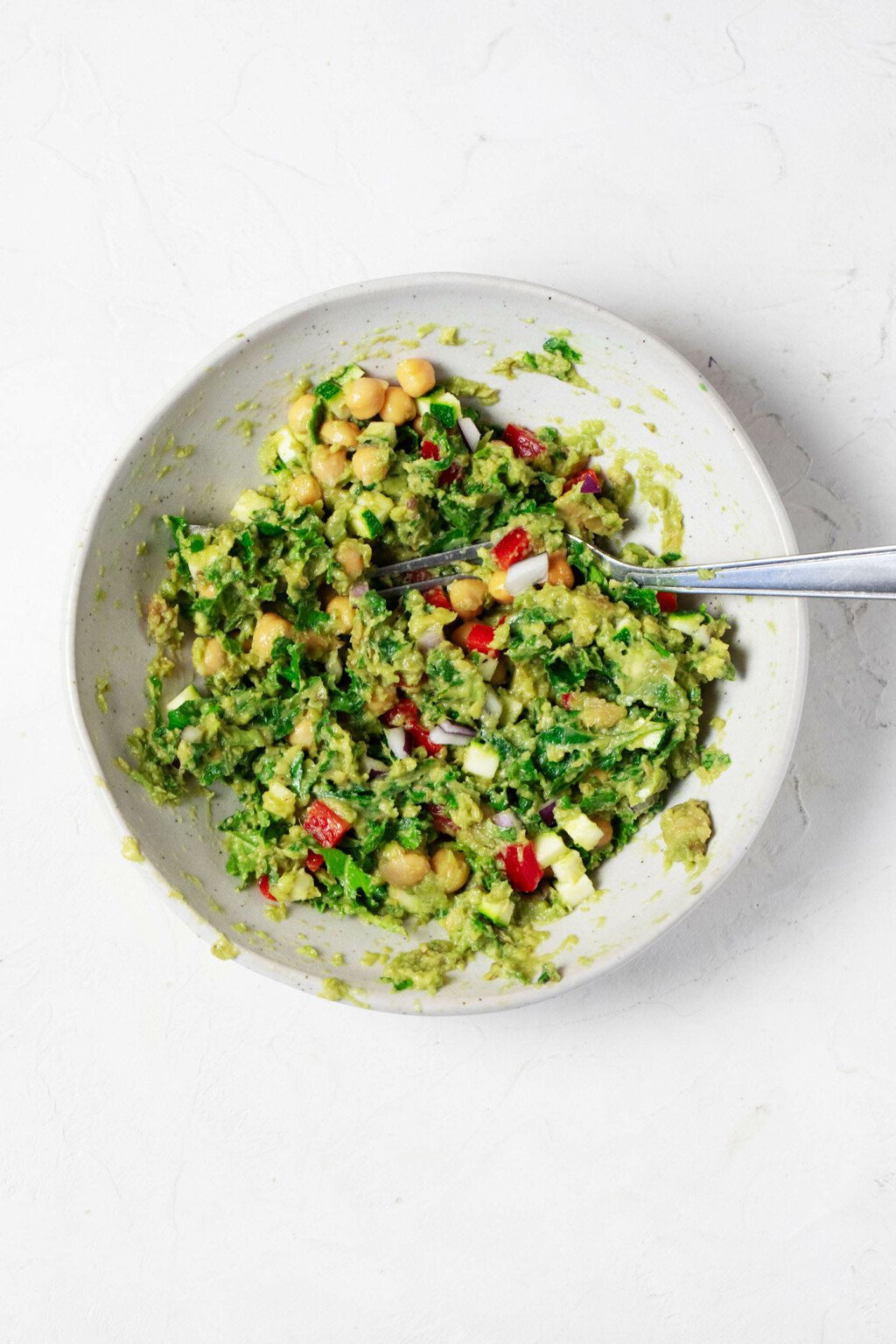 An overhead image of a bowl of guacamole that has been made more colorful with the addition of various chopped vegetables and chickpeas.