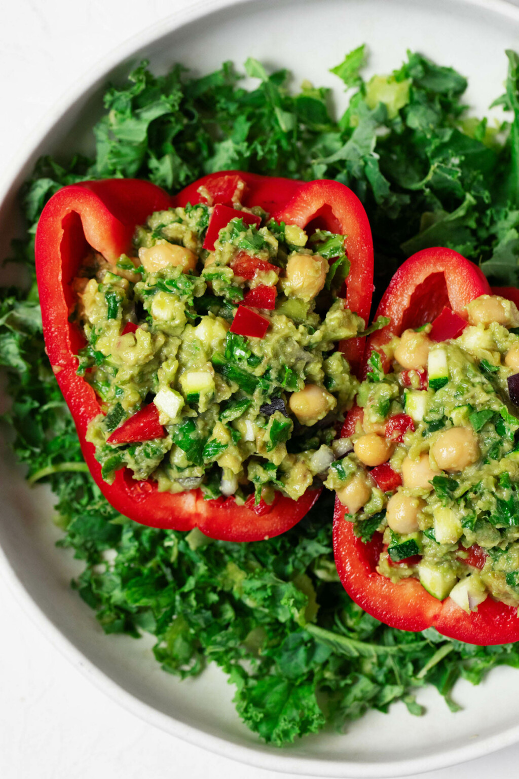 Two guacamole stuffed pepper halves have been arranged over a bright green bed of kale. 