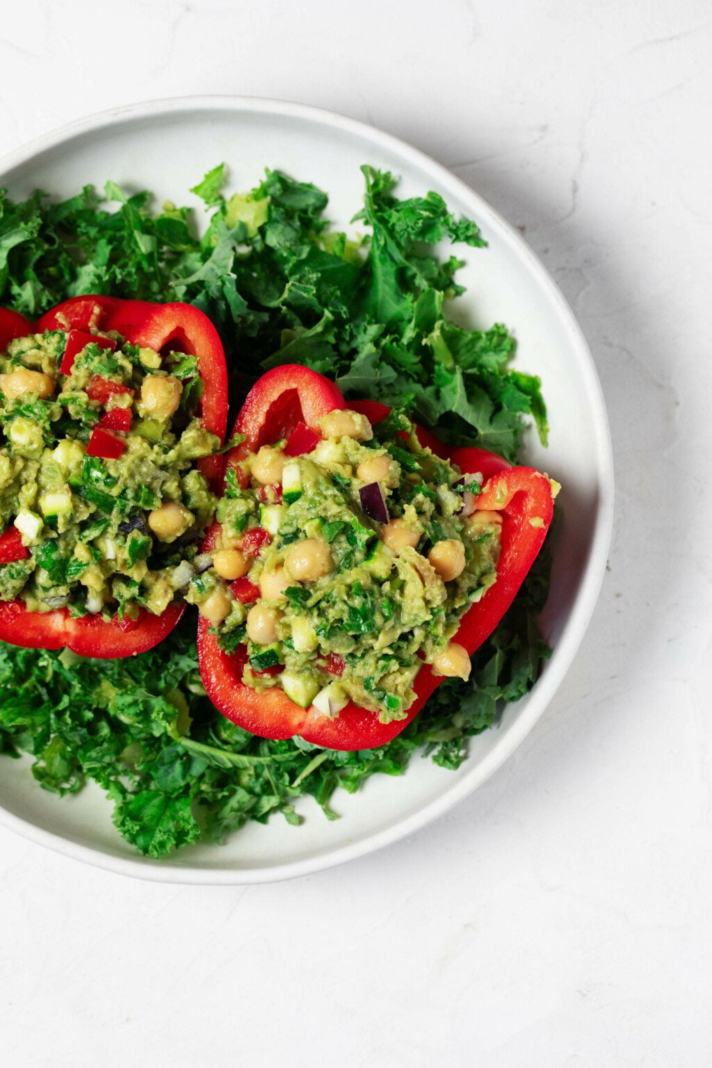 An overhead image of two red pepper halves, which have been filled with a colorful mixture of guacamole, chickpeas, and vegetables.