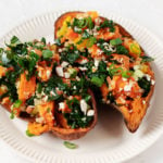 Two baked sweet potatoes have been stuffed with a colorful mixture of kale, raw vegetables, and almonds.
