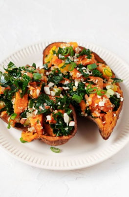 Two baked sweet potatoes have been stuffed with a colorful mixture of kale, raw vegetables, and almonds.