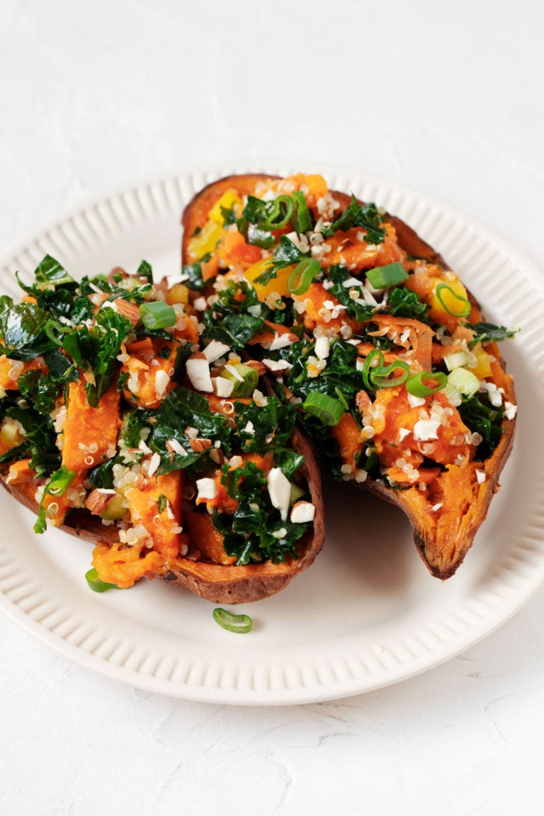 Two baked sweet potatoes have been stuffed with a colorful mixture of kale, raw vegetables, and almonds.