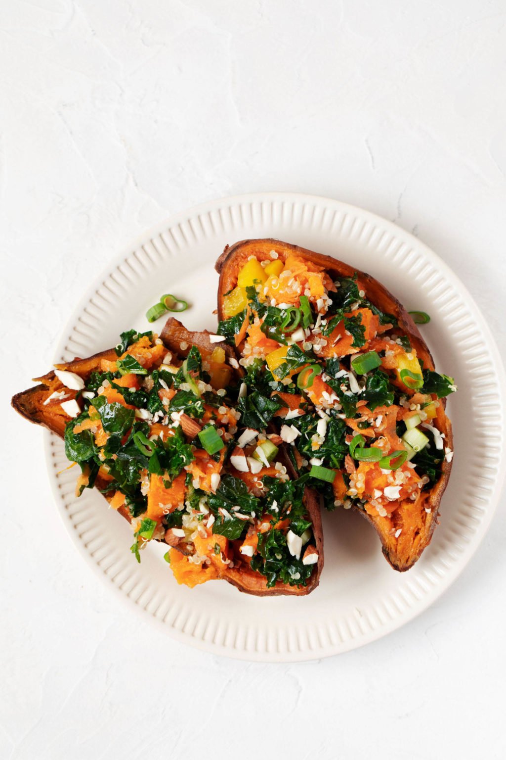 A white, cream-colored, fluted plate holds two stuffed sweet potato skins. They're filled with a colorful vegetable salad.