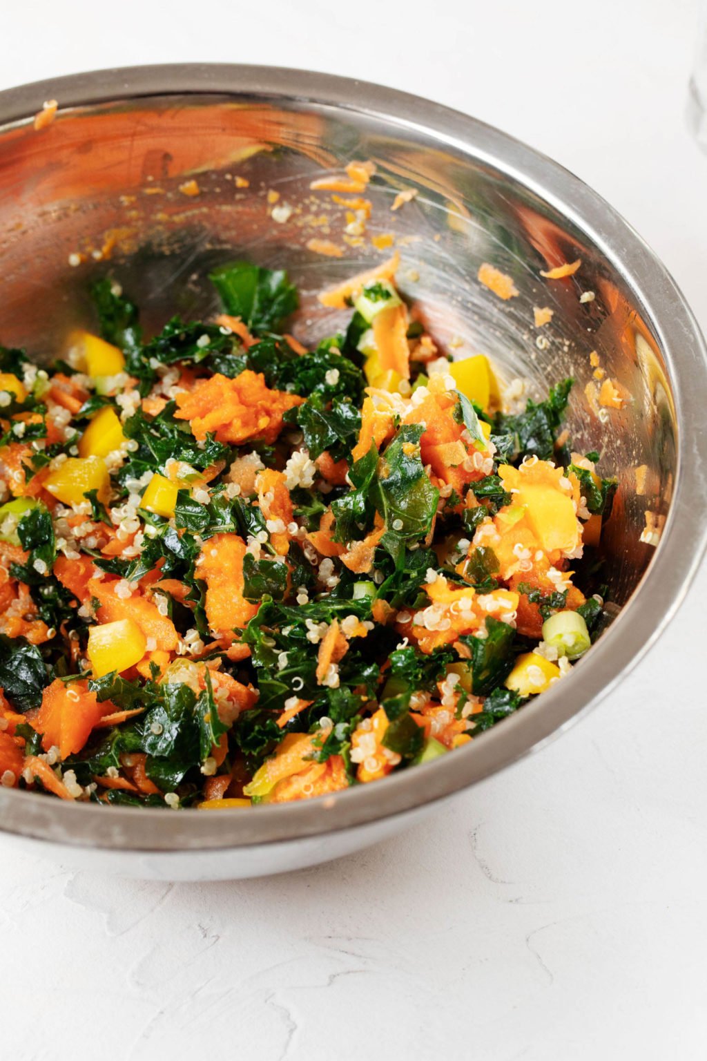 A large, stainless steel mixing bowl is filled with colorful, plant-based ingredients.