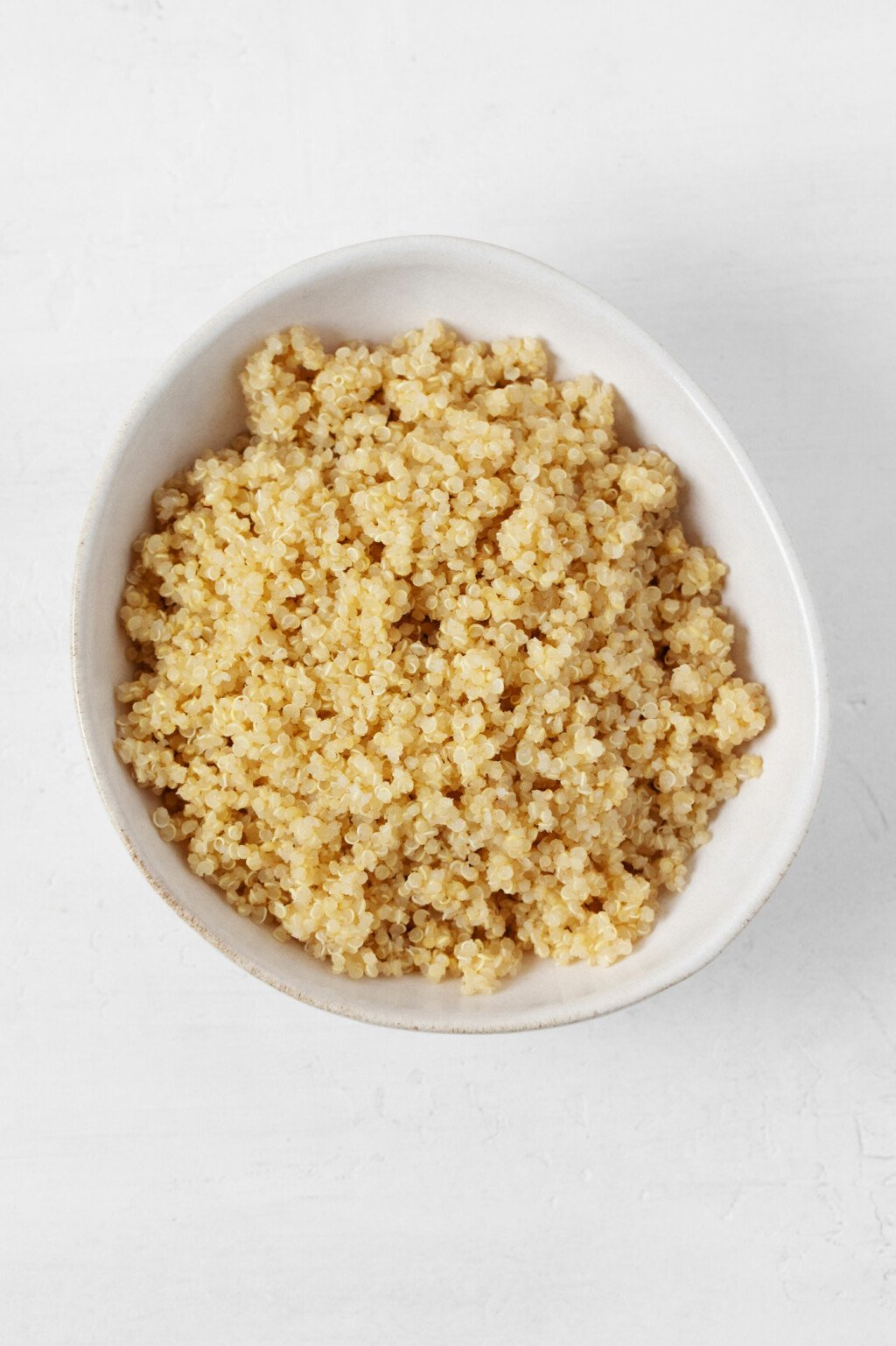 An asymmetrical, white bowl is filled with fluffy cooked quinoa.