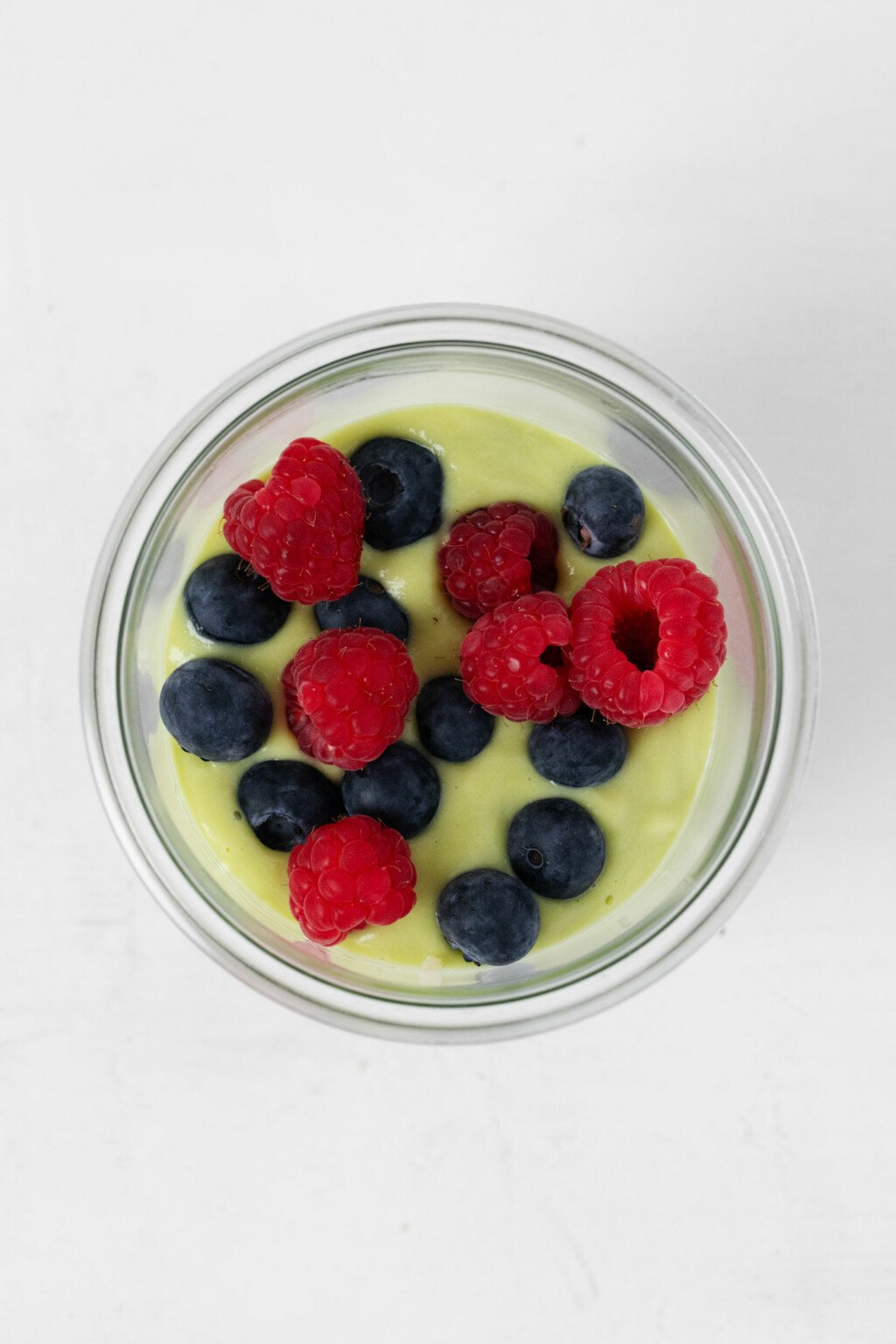 An overhead image of a pale green, avocado vanilla pudding topped with red and blue berries.