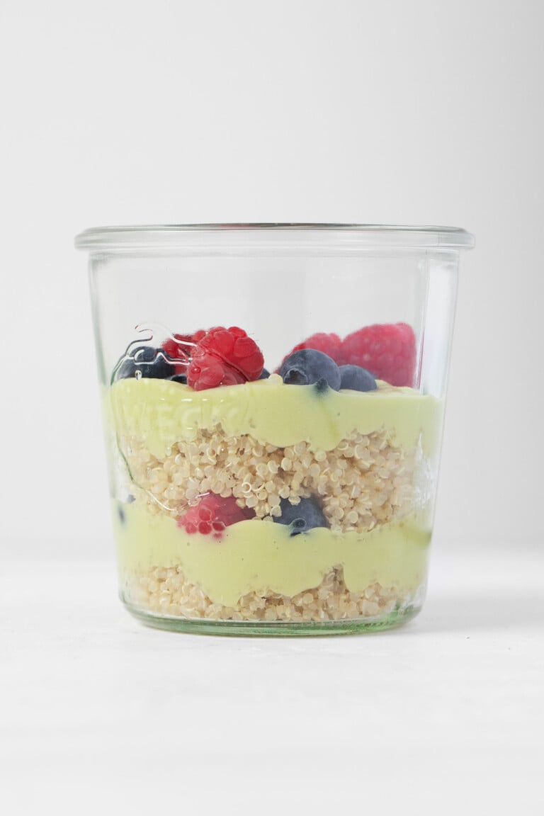 A weck mason jar is filled with layers of cooked quinoa, berries, and a creamy, vanilla lemon avocado pudding.