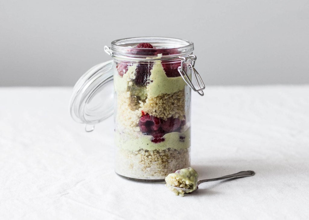 A clear mason jar is filled with layers of quinoa, avocado cream, and berries.