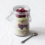 A glass mason jar holds a quinoa breakfast parfait with berries and avocado cream. It rests on a white cloth.