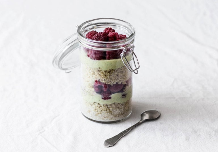 A glass mason jar holds a quinoa breakfast parfait with berries and avocado cream. It rests on a white cloth.