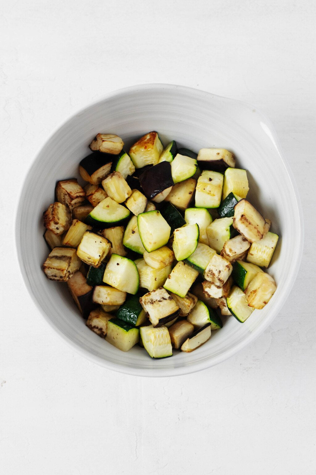 Roasted zucchini has been piled into a round, white ceramic bowl.