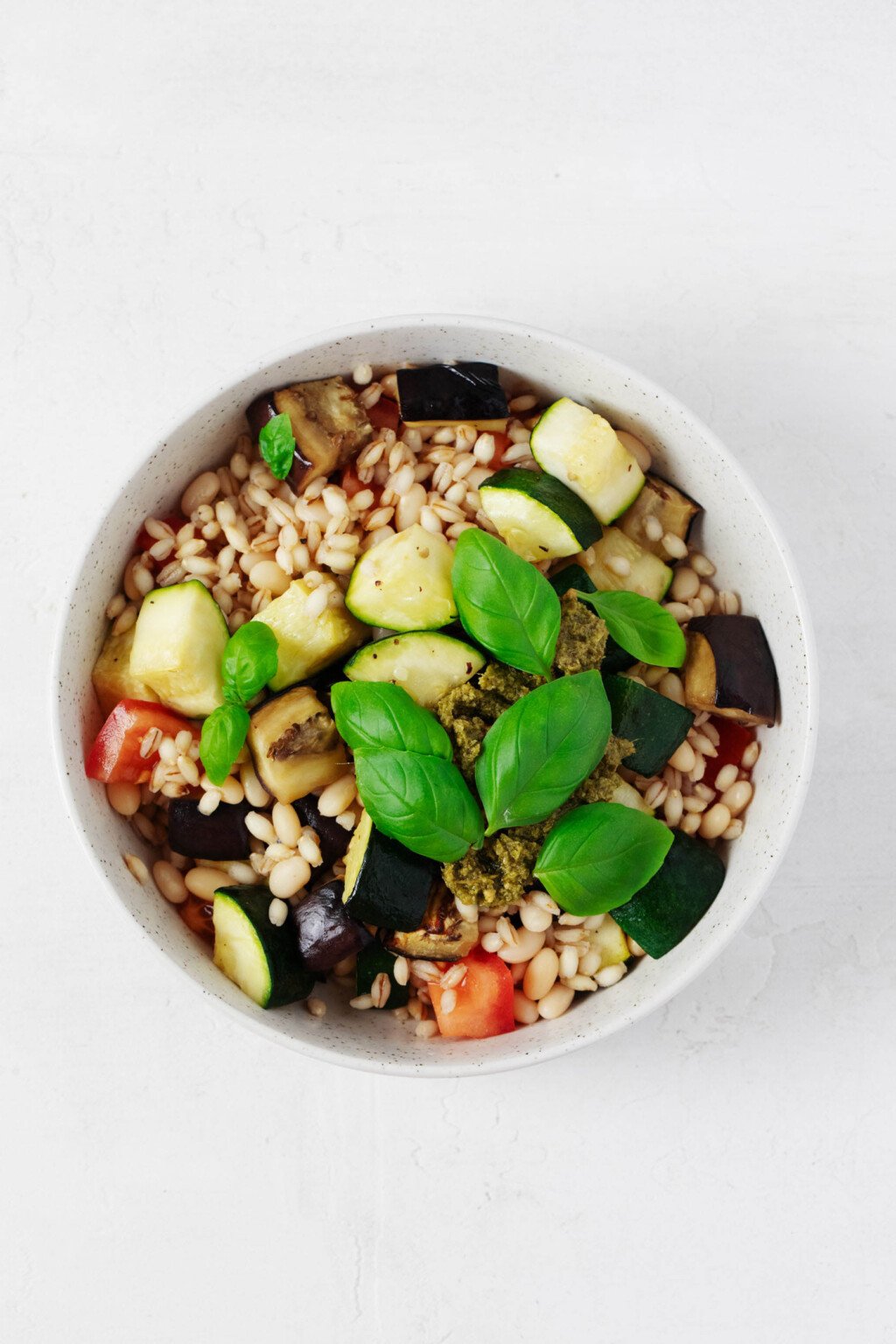 Vegan pesto bowls, consisting of white beans, barley, roasted vegetables, and plant-based pesto, are served on a white surface.