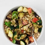 Vegan pesto bowls, consisting of white beans, barley, roasted vegetables, and plant-based pesto, are served on a white surface.