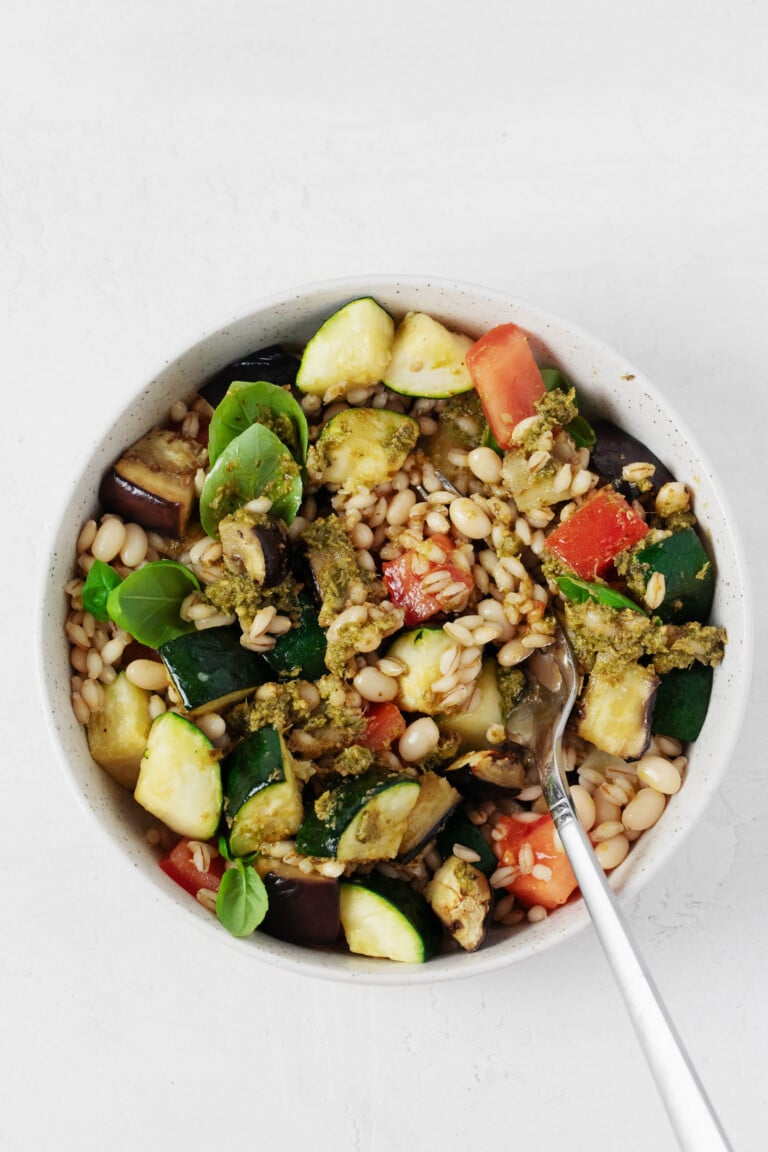 Vegan pesto bowls, consisting of white beans, barley, roasted vegetables, and plant-based pesto, are served on a white surface.