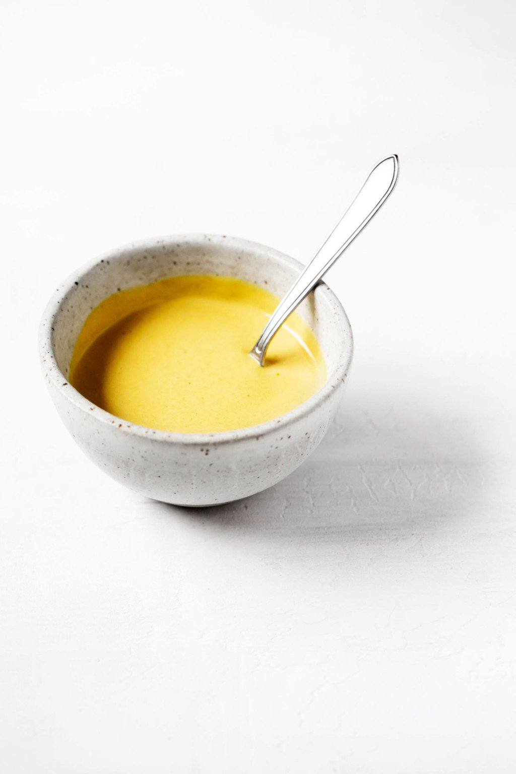 A small, ceramic pinch bowl contains a vegan turmeric tahini dressing, which is a bright golden color.