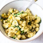 A round, white bowl has been filled with a mixture of scrambled tofu and thinly sliced, green zucchini.