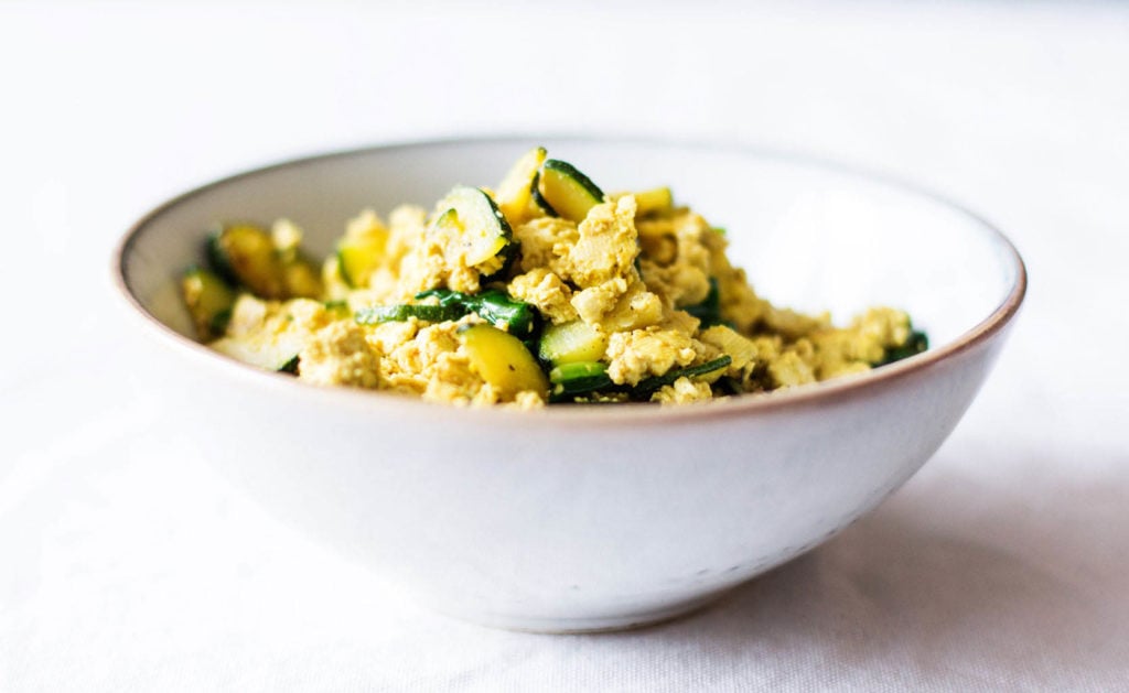 An angled image of a white bowl, which has been filled with crumbled tofu, spices, and vegetables.