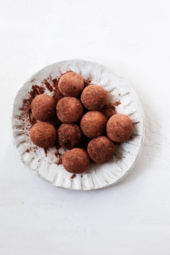 A plate of raw vegan brownie bites, rolled in cacao powder to resemble truffles.