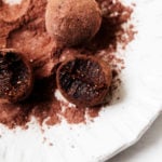 Sweet, luscious raw vegan brownie bites, freshly dusted in cacao powder and served on a plate.