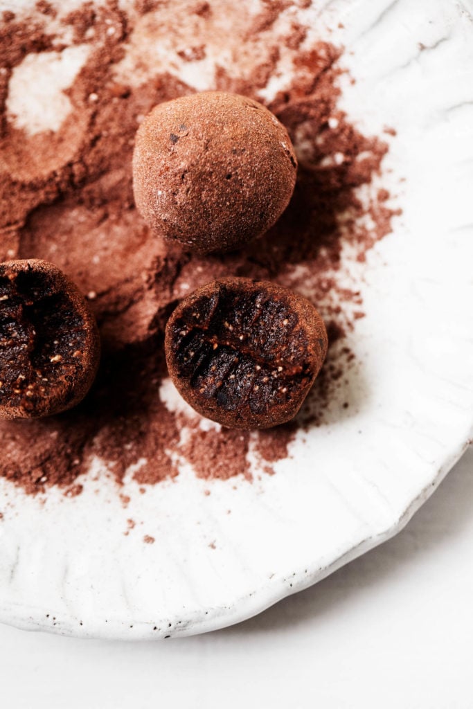 Sweet, luscious raw vegan brownie bites, freshly dusted in cacao powder and served on a plate.