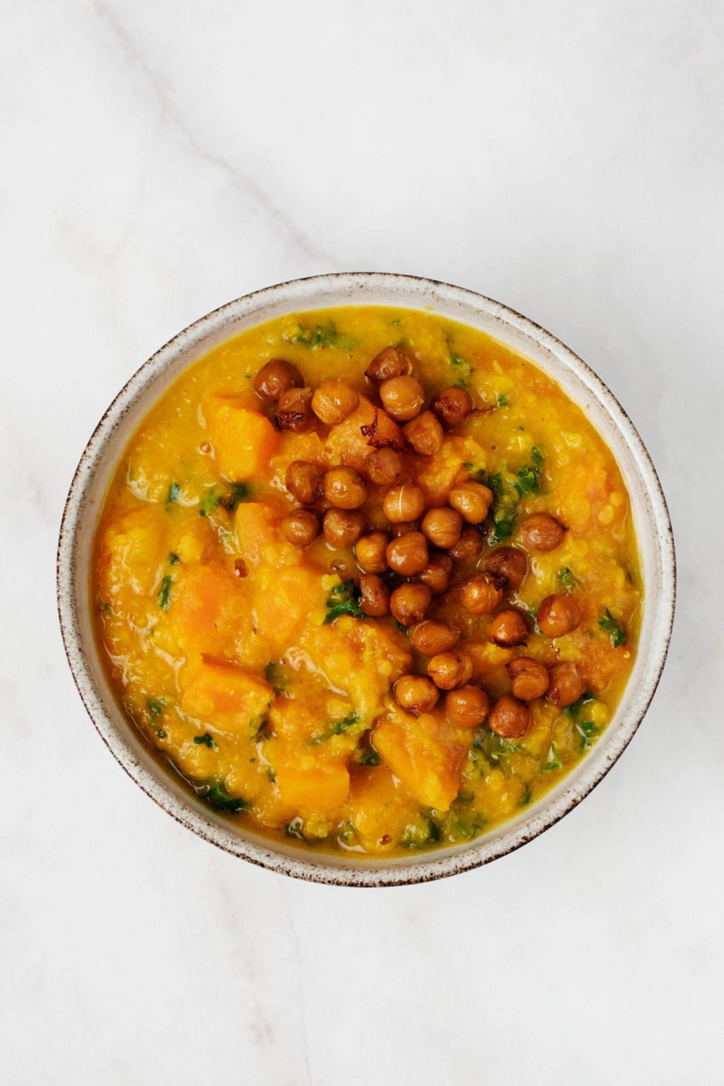 A bowl of red lentil butternut soup has been topped with crispy roasted chickpeas.