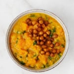 A bowl of red lentil butternut soup has been topped with crispy roasted chickpeas.
