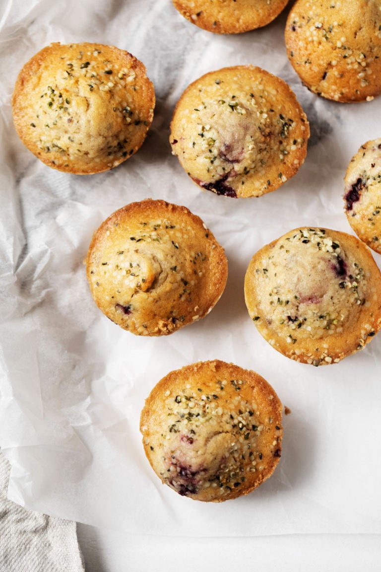Nutritious, freshly baked berry hemp spelt muffins, sprinkled with shelled hemp seeds and resting on parchment paper.