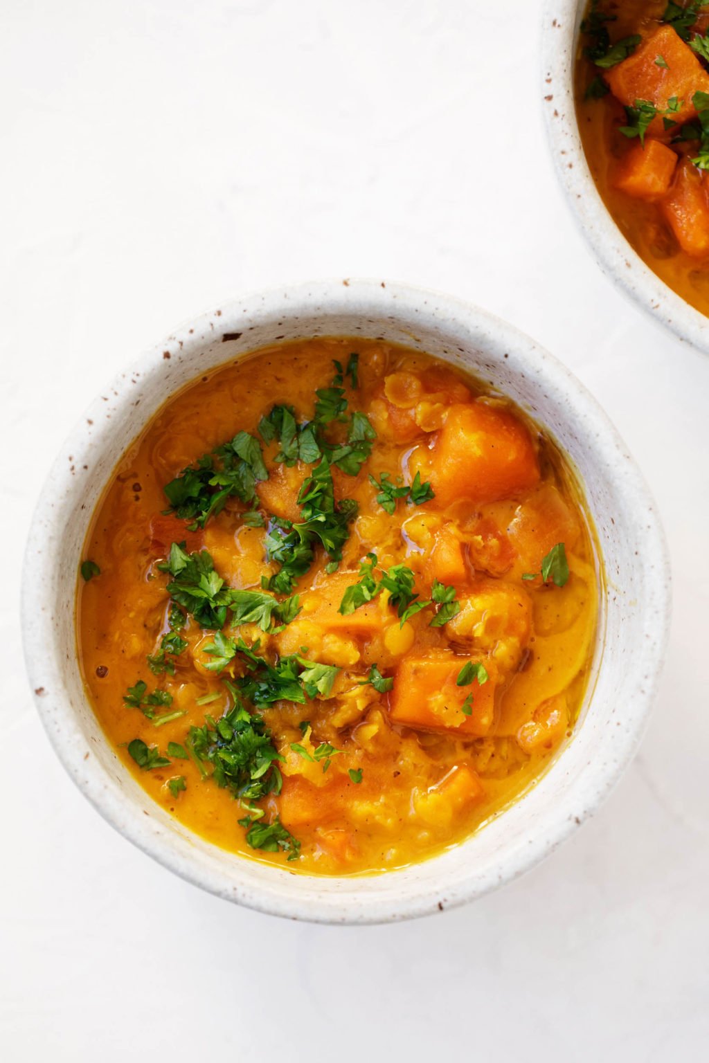 Two small stoneware bowls contain a vibrant, orange colored mixture of curried sweet potato lentils.