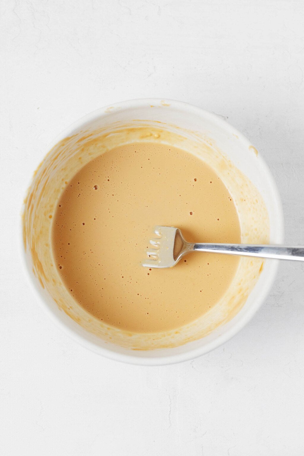 A creamy peanut dressing is pictured overhead in a small white bowl.