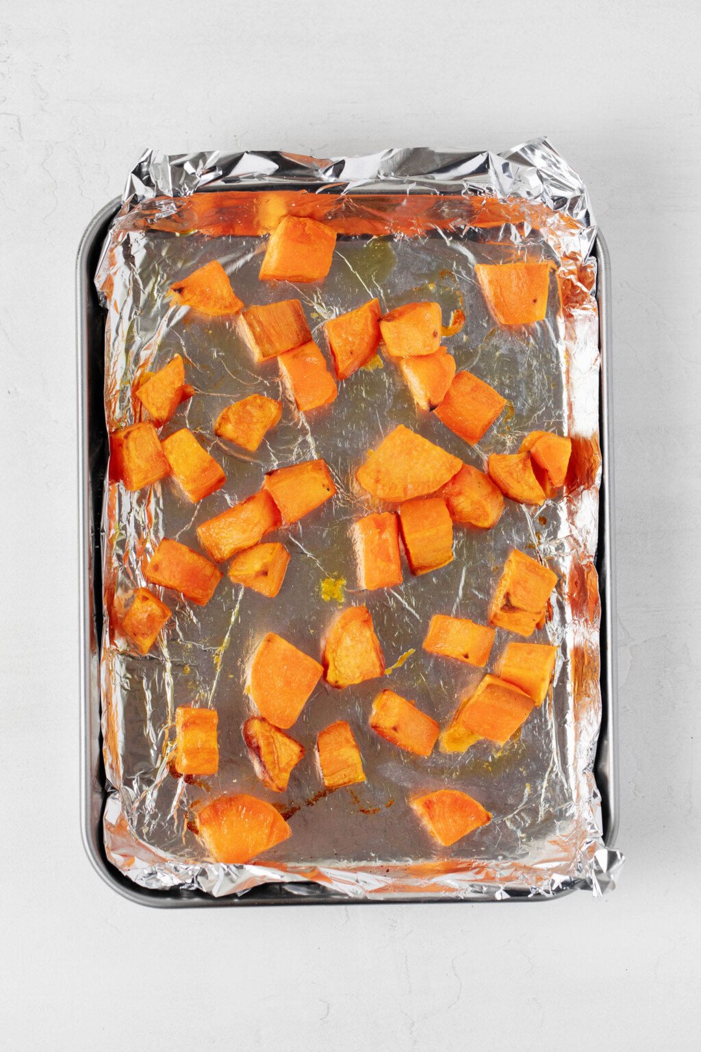 An overhead image of cubed sweet potatoes on a silver, aluminum-lined baking sheet.