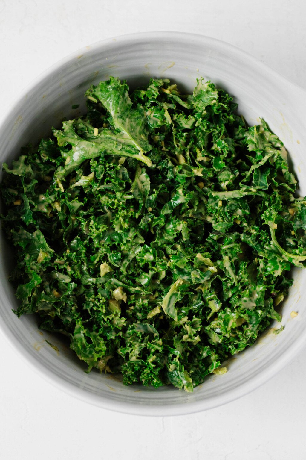 An overhead image of kale, which is coated in a creamy dressing, in a white mixing bowl.