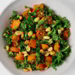 A spicy peanut kale salad with roasted sweet potato cubes is pictured in a large white mixing bowl.